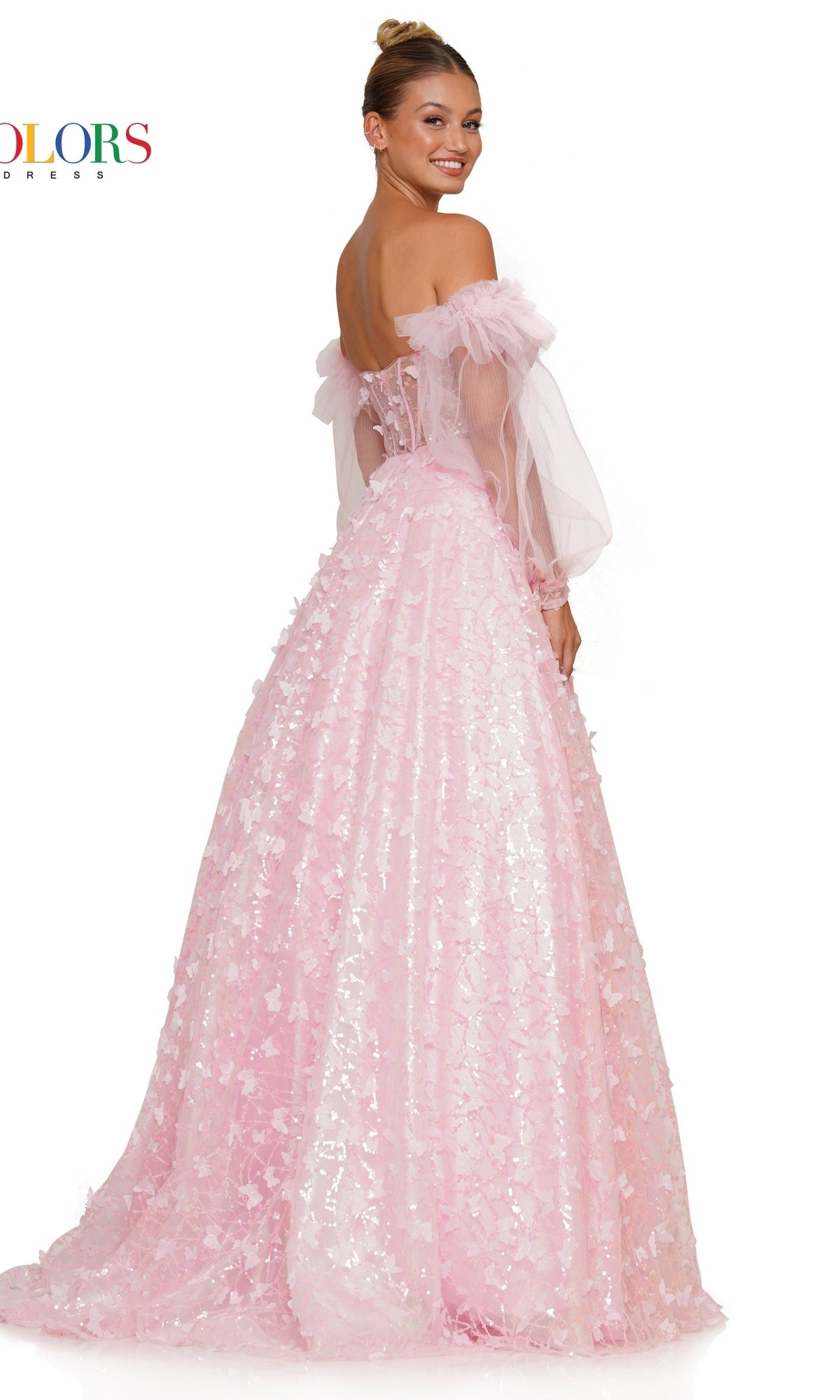 A woman poses and smiles over her shoulder wearing the 3D Butterfly Formal Ball Gown 3226 with sleeves—a light pink, off-the-shoulder dress featuring removable sheer puff sleeves and a textured floral butterfly pattern.